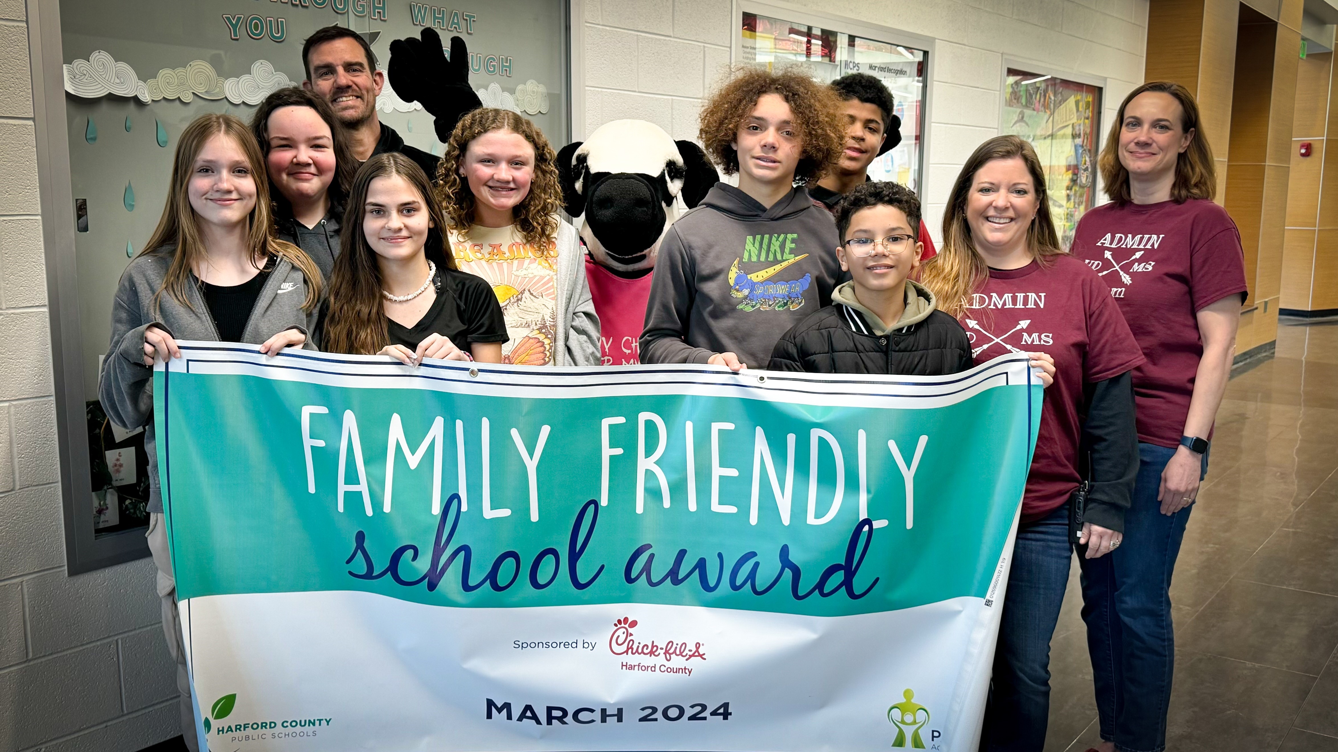 School leaders, students, and Chick-fil-A mascot hold up March 2024 Family Friendly School Award banner.