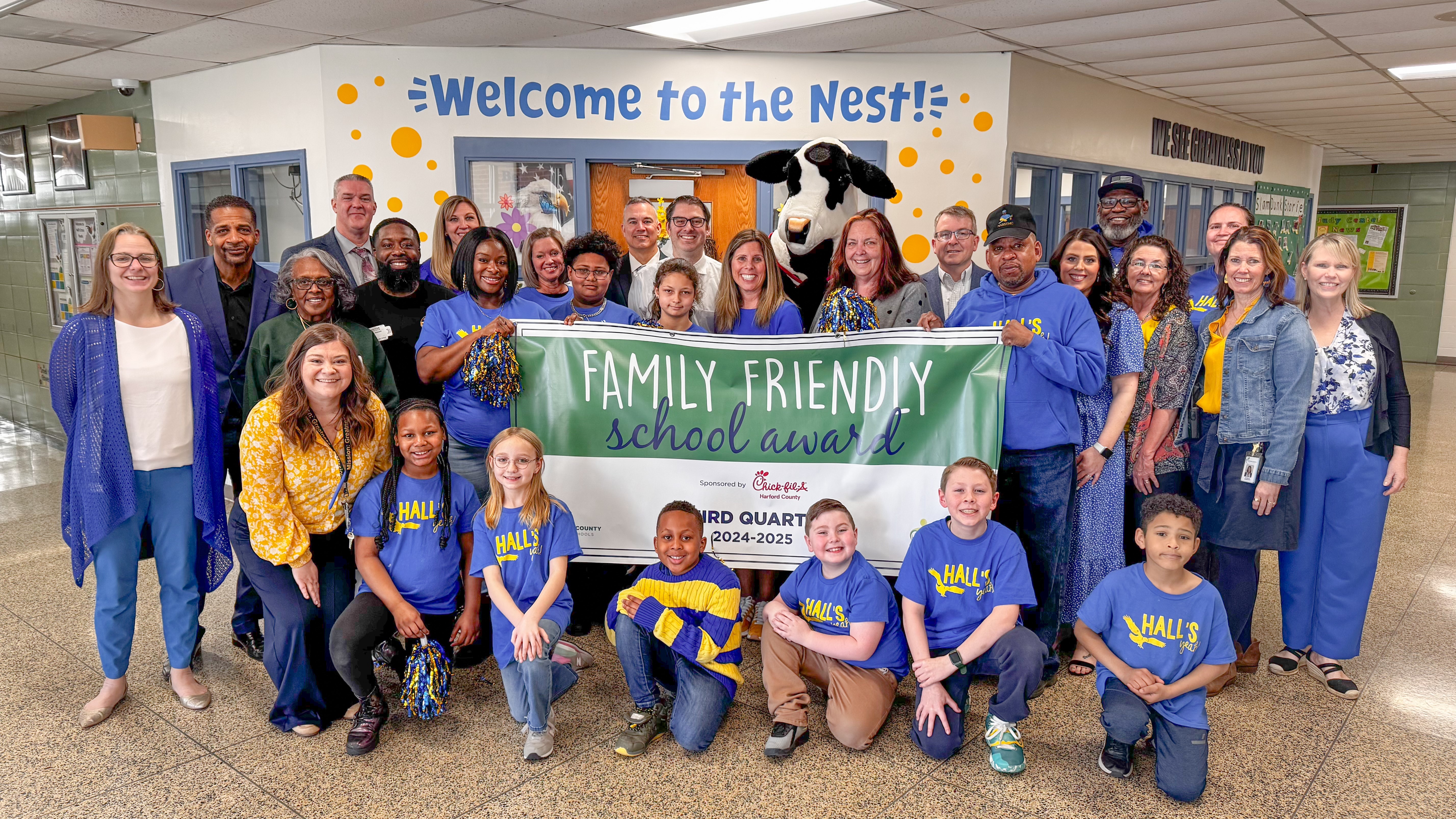 School system leaders, students, and Chick-fil-A mascot hold up Third Quarter Family Friendly School Award banner.