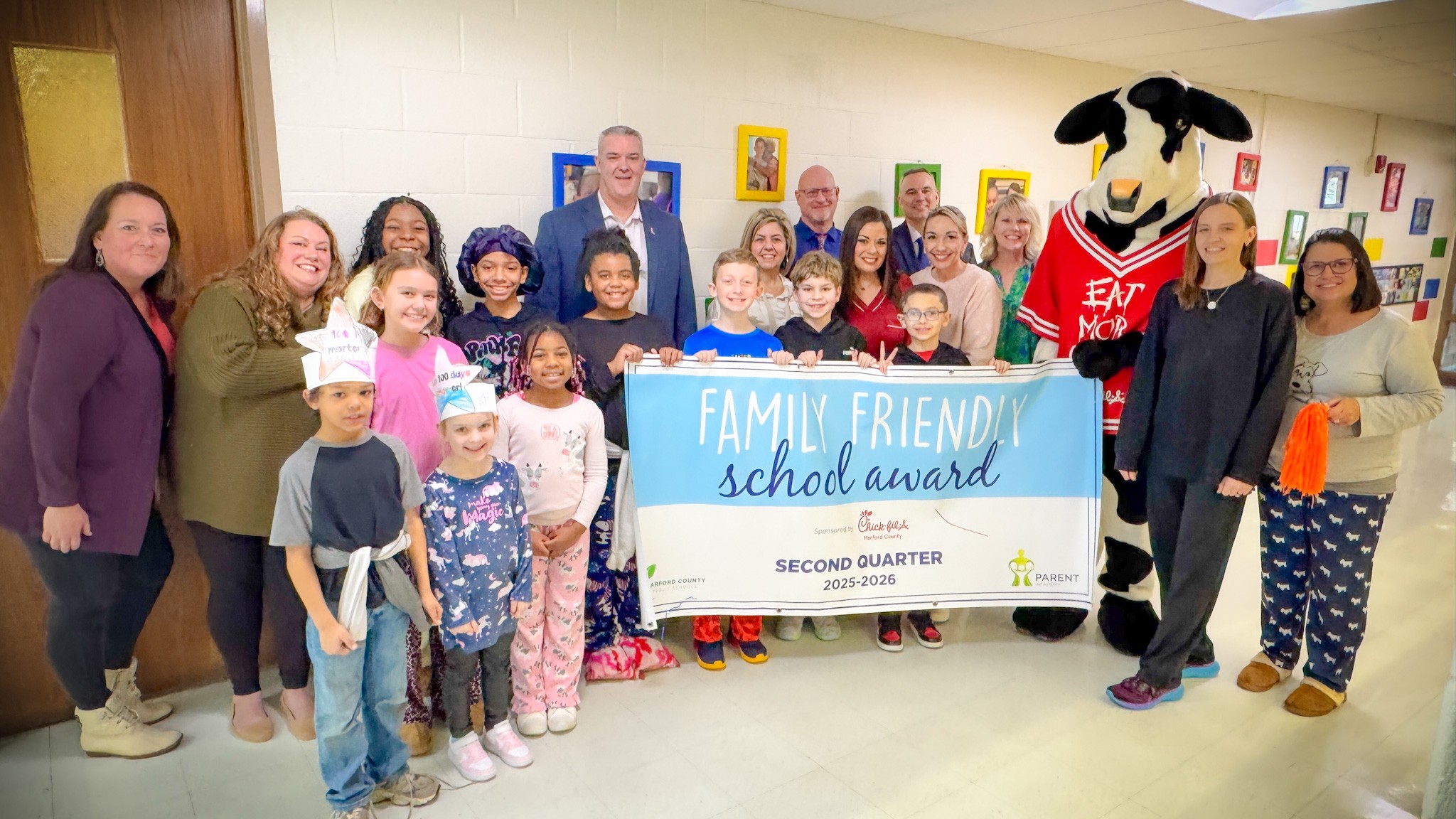 School system leaders, students, and Chick-fil-A mascot hold up Second Quarter Family Friendly School Award banner.