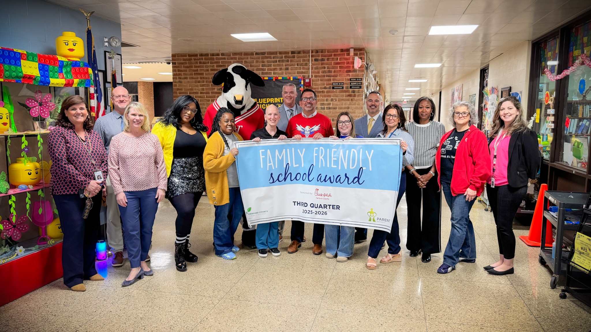 School system leaders, students, and Chick-fil-A mascot hold up Third Quarter Family Friendly School Award banner.