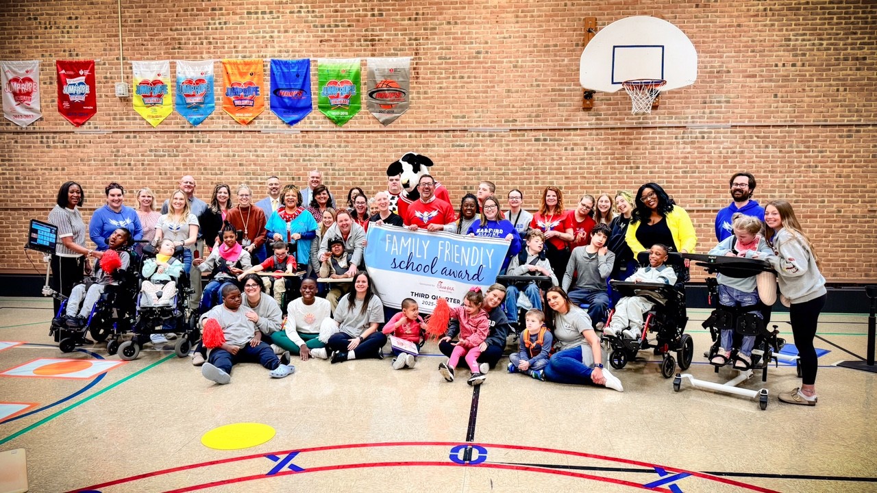 School system leaders, students, and Chick-fil-A mascot hold up Third Quarter Family Friendly School Award banner.