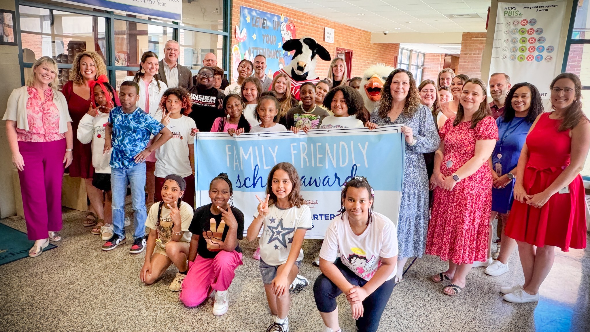 School system leaders, students, and Chick-fil-A mascot hold up Fourth Quarter Family Friendly School Award banner.