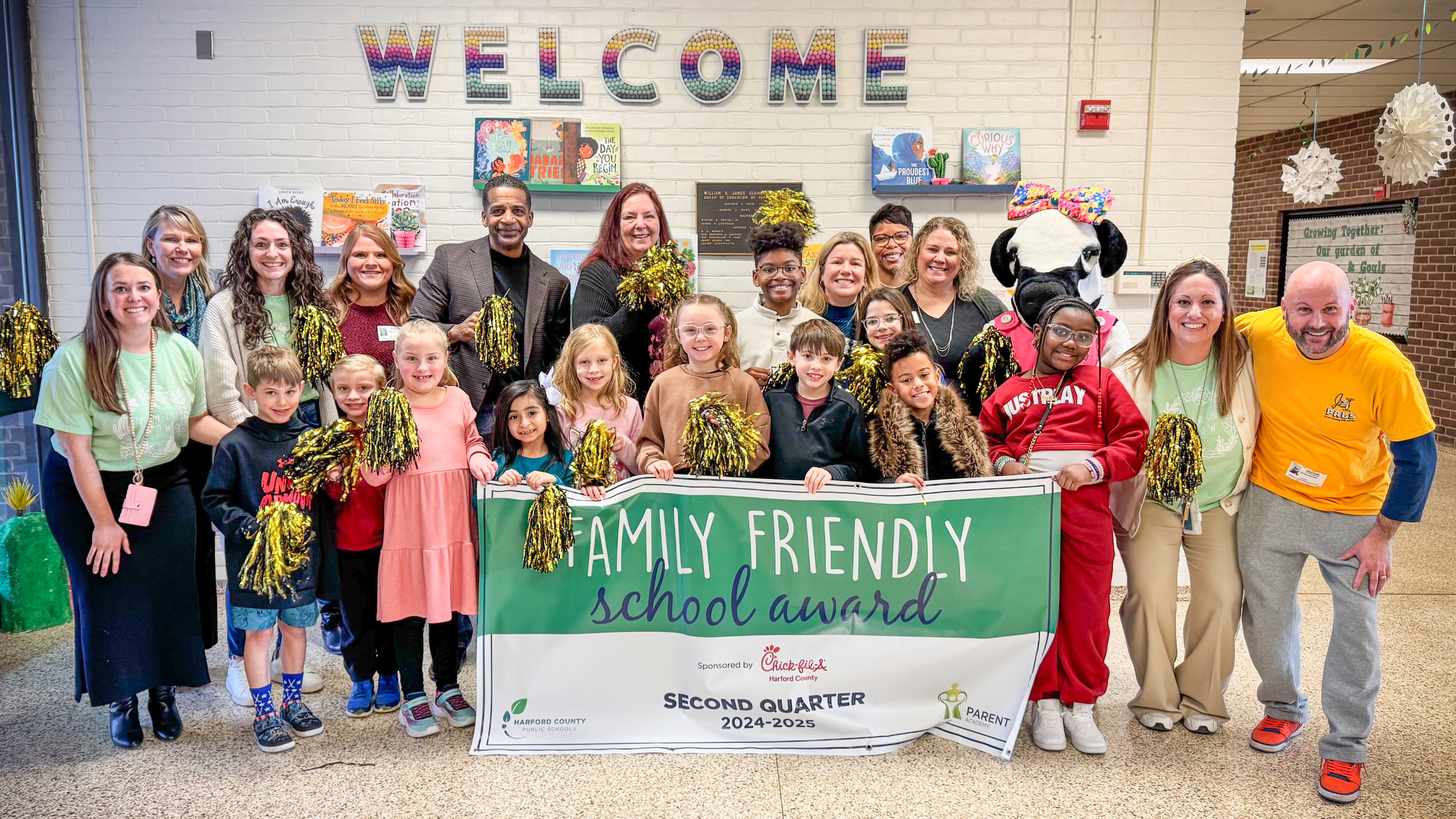 School system leaders and students and Chick-fil-A mascot hold up Quarter 2 Family Friendly School Award banner.